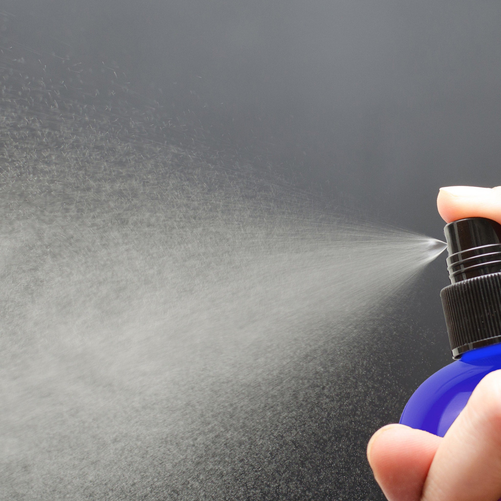 Spray bottle, blue plastic bottle with black cap, spraying water mist