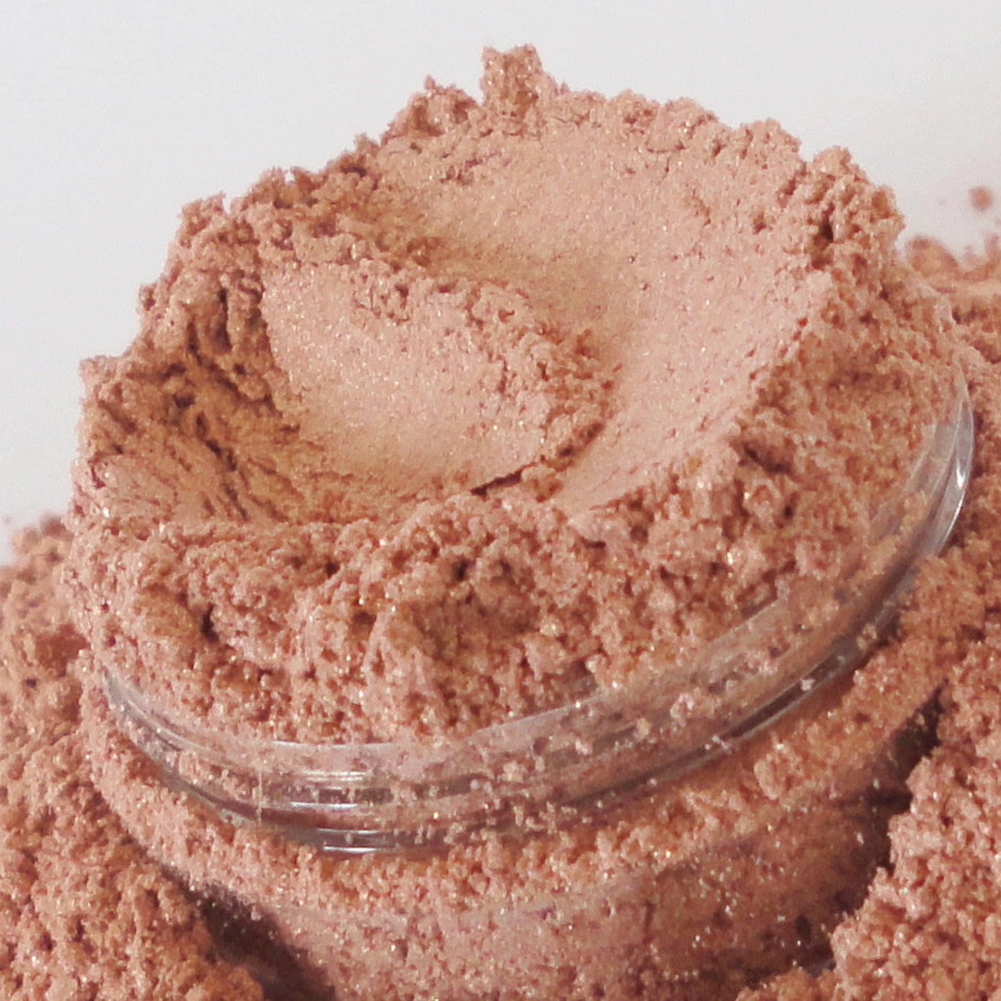 Powdered cosmetic product in pink with glitter, inside a clear plastic container
