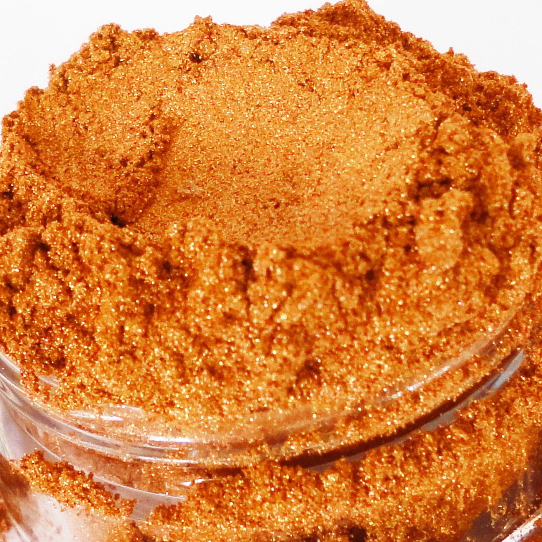 Orange glitter powder in a clear glass jar, with sparkling texture and fine granules