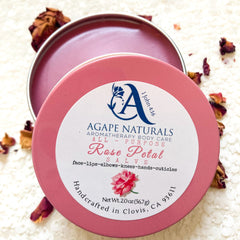 Rose petal salve in pink tin with white label, "Agape Naturals" brand visible, surrounded by petals