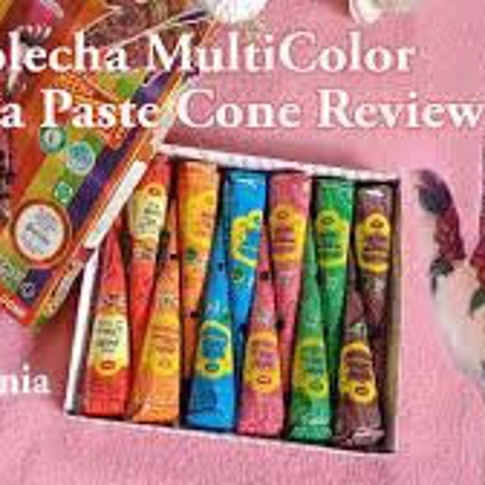 Six vibrant vegan henna paste cones in purple, red, magenta, orange, green, and blue arranged on marble surface