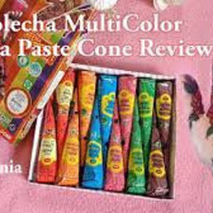 Six vibrant vegan henna paste cones in purple, red, magenta, orange, green, and blue arranged on marble surface