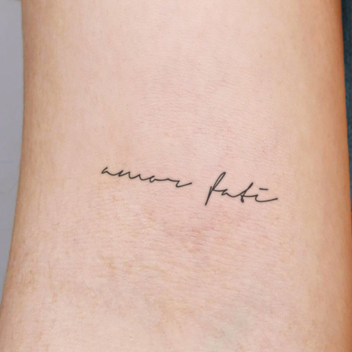 Three sleek black tubes of Amor Fati temporary tattoo ink with gold accents, arranged diagonally on marble surface