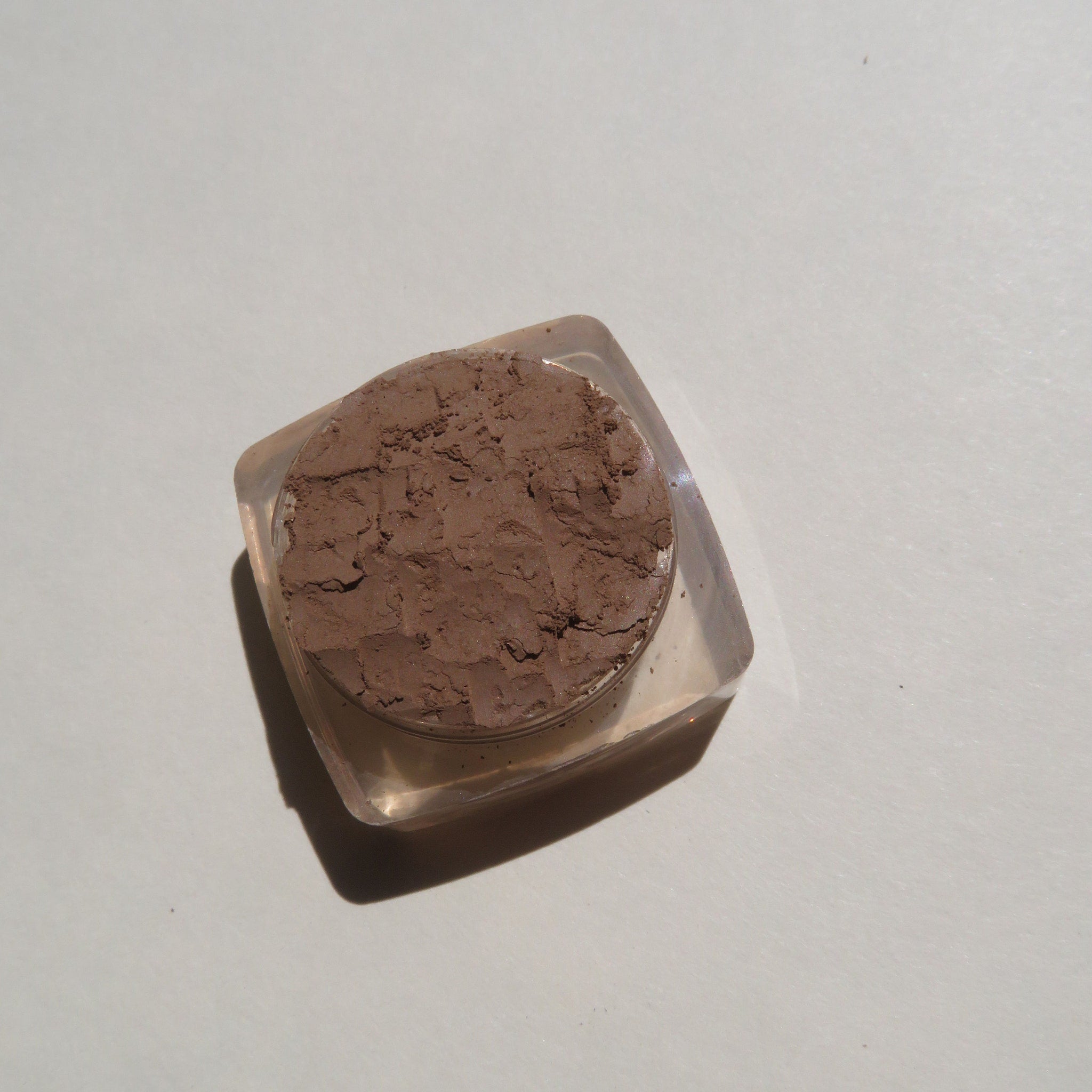 Close-up of loose mineral eyeshadow in matte medium brown with soft powdery texture and vegan label visible