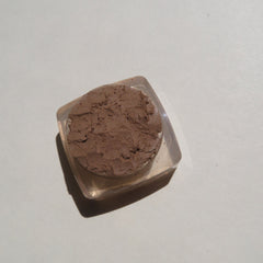 Close-up of loose mineral eyeshadow in matte medium brown with soft powdery texture and vegan label visible