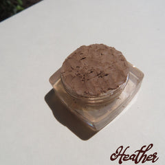 Close-up of loose mineral eyeshadow in matte medium brown shade with vegan label, displayed in open jar
