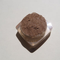 Hand applying loose mineral eyeshadow in matte brown shade with a fluffy brush onto eyelid