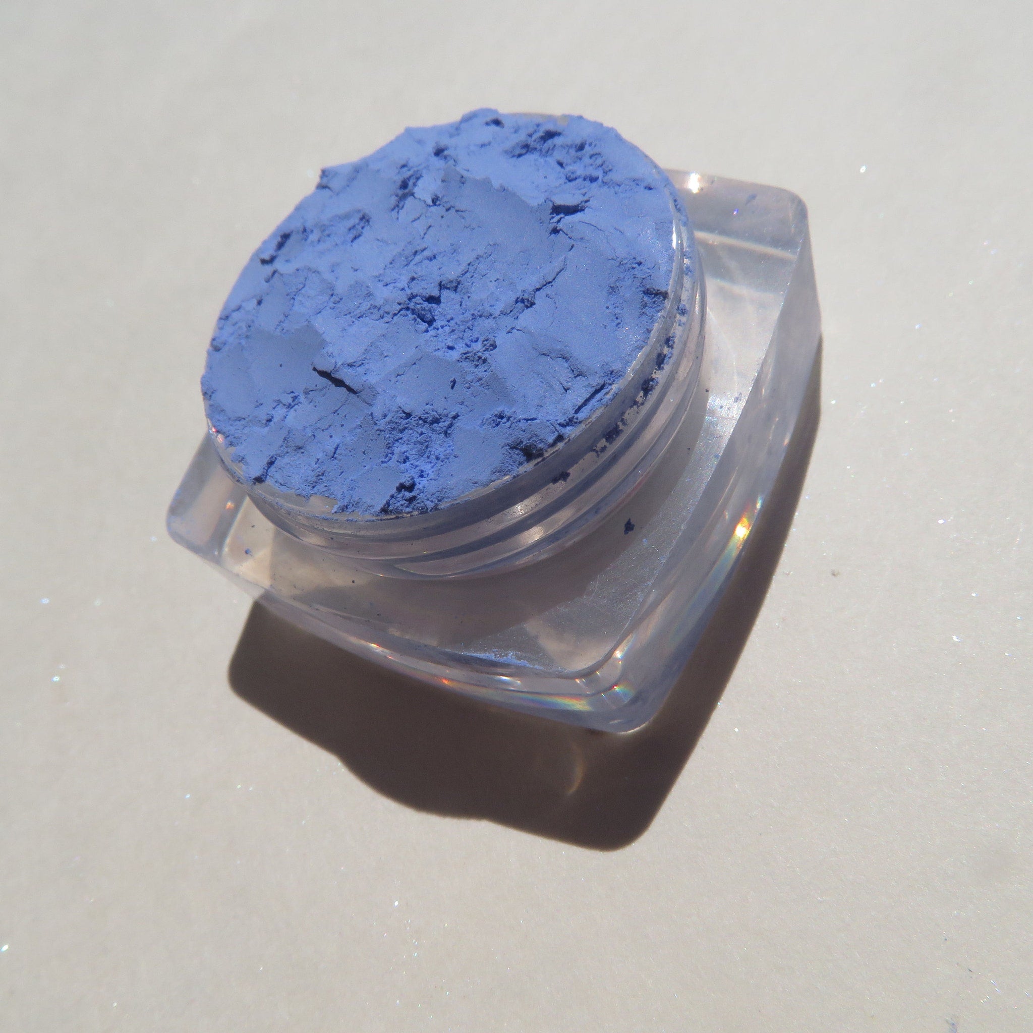Close-up of matte sky blue loose mineral eyeshadow pigment with soft powdery texture in a small jar
