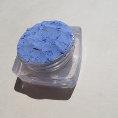 Side view of matte sky blue loose mineral eyeshadow in a clear jar with black screw-top lid, showcasing fine powder texture.