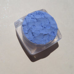 Close-up of vibrant matte sky blue loose mineral eyeshadow powder with smooth texture in a small jar