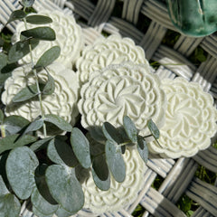 White floral-patterned soaps with eucalyptus leaves on a woven basket