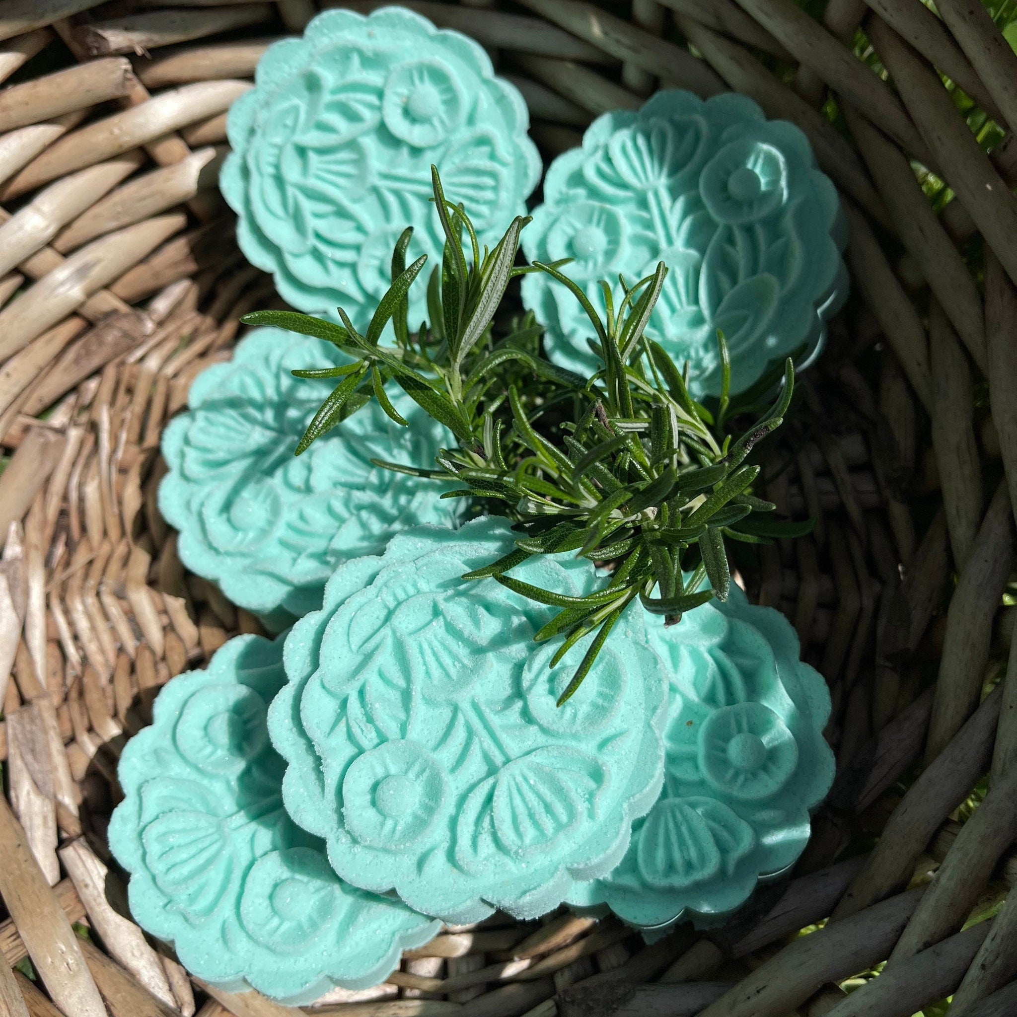 Floral-shaped teal soap with embossed floral pattern and rosemary sprig in woven basket