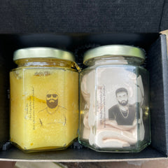 Body scrub and whipped cream jars with yellow and pink contents, gold lids, and black box packaging