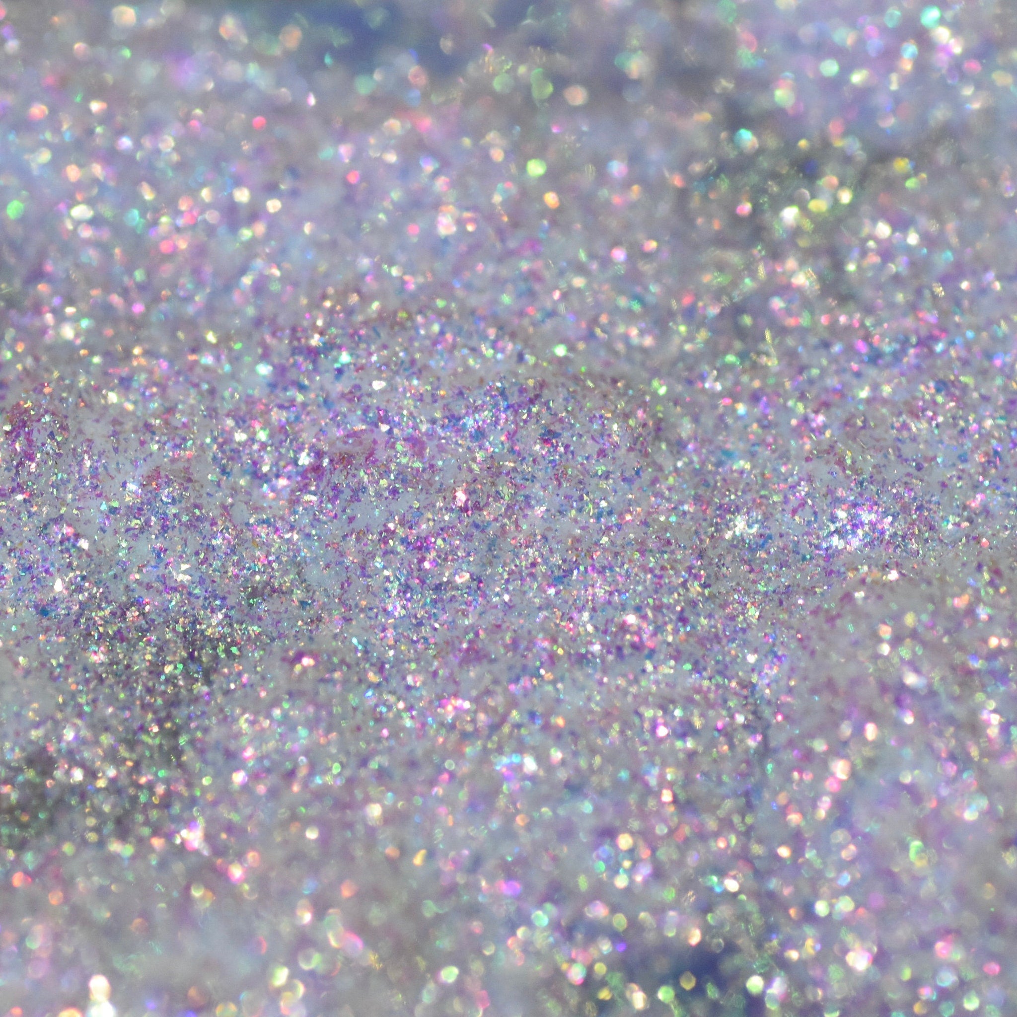 Open jar of Moon Dust loose powder eyeshadow with multichrome shimmer and silver scoop on marble surface