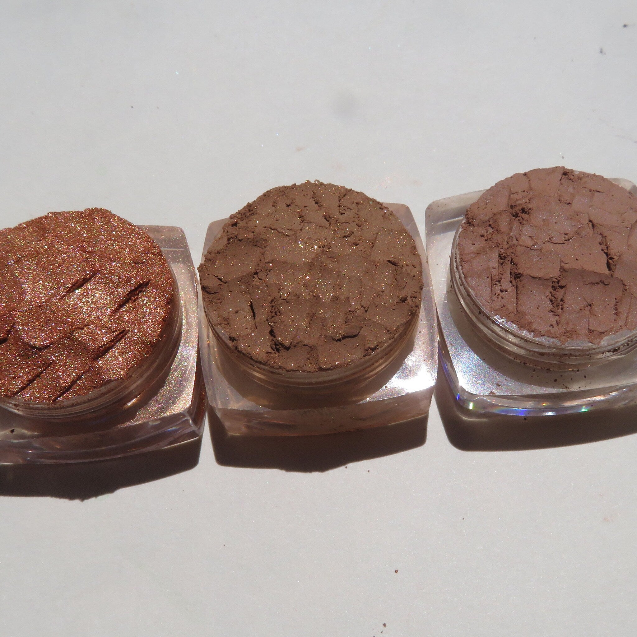 Hand applying shimmery Tigerlily brown eyeshadow to eyelid with fingertip, showcasing rich pigment blend