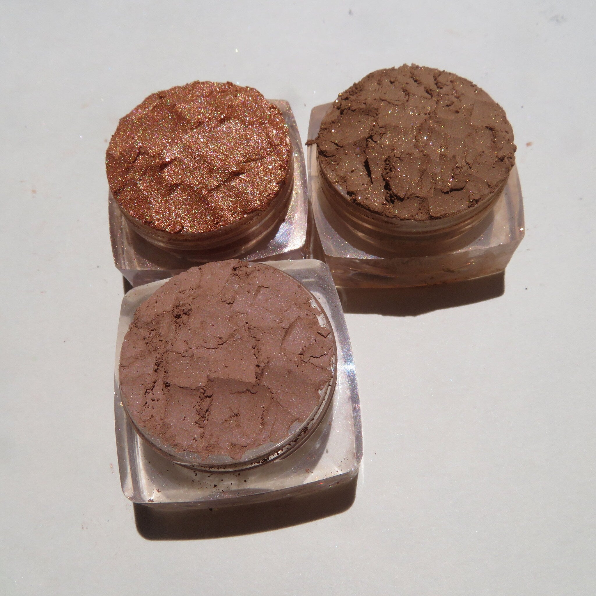 Side view of three round mineral eyeshadow pans in fall brown shades: matte basic, shimmer showstopper, and metallic tigerlily