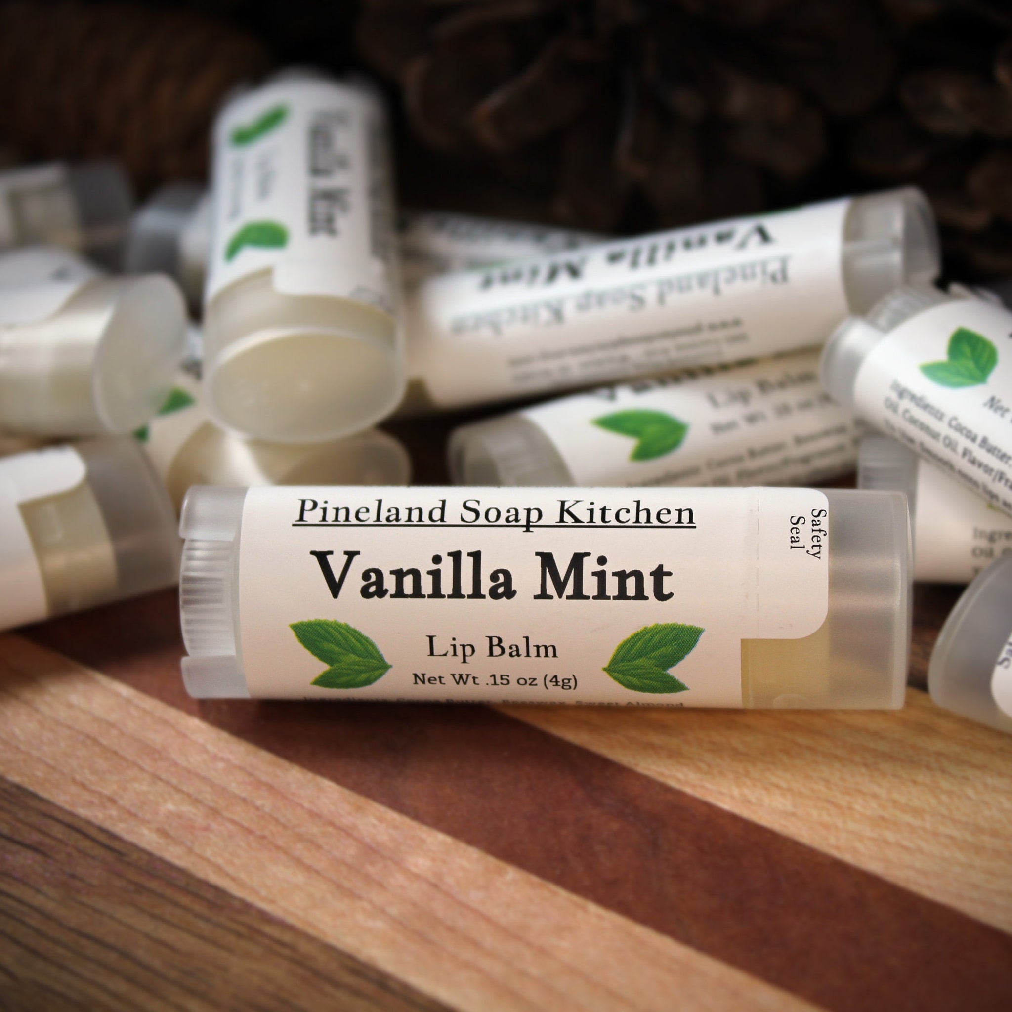 Lip balm tubes with white labels, green leaf design, and "Vanilla Mint" text, by Pineland Soap Kitchen on wood surface