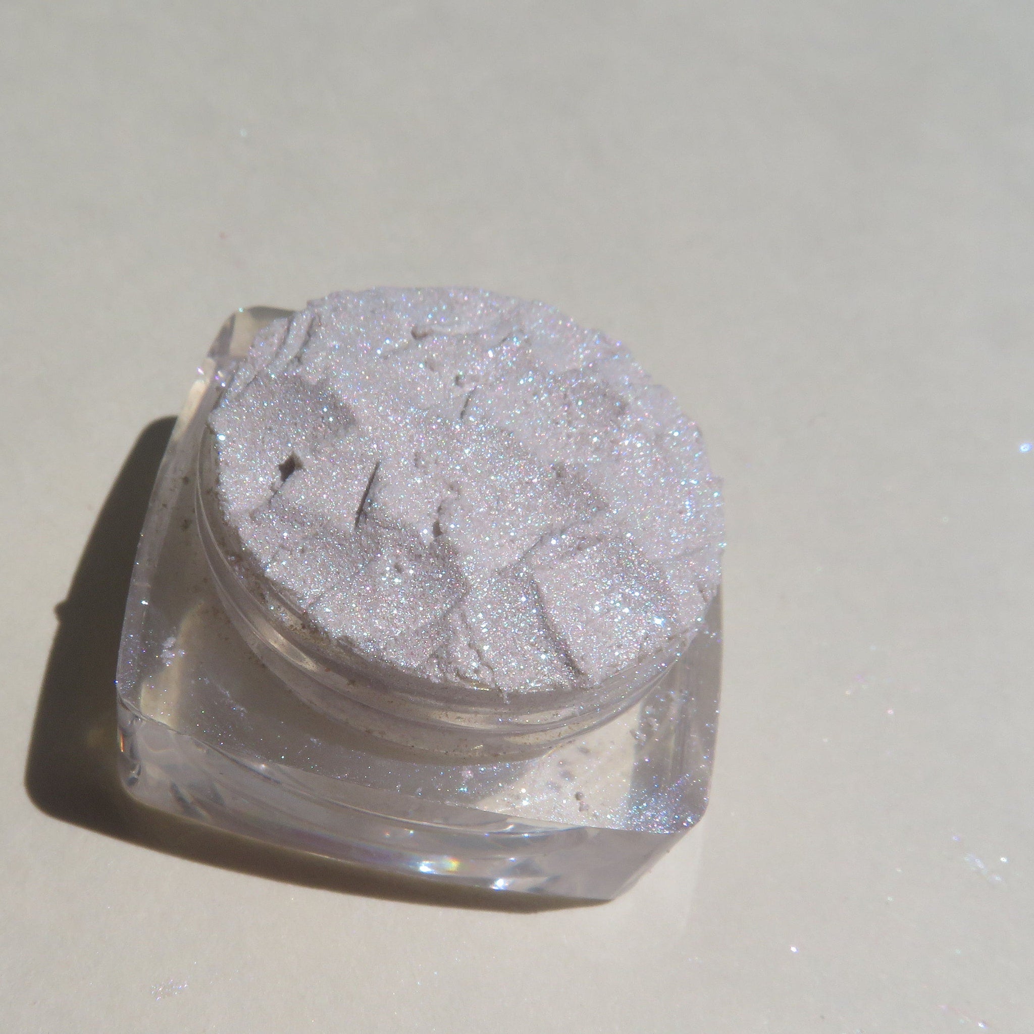 Close-up of loose white and taupe glitter eye shadows with shimmer particles in small glass jars