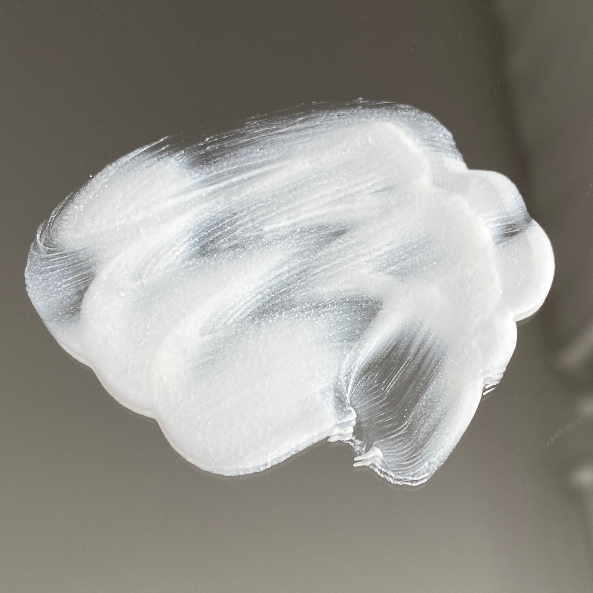 White cream swatch with textured brushstrokes on a reflective surface