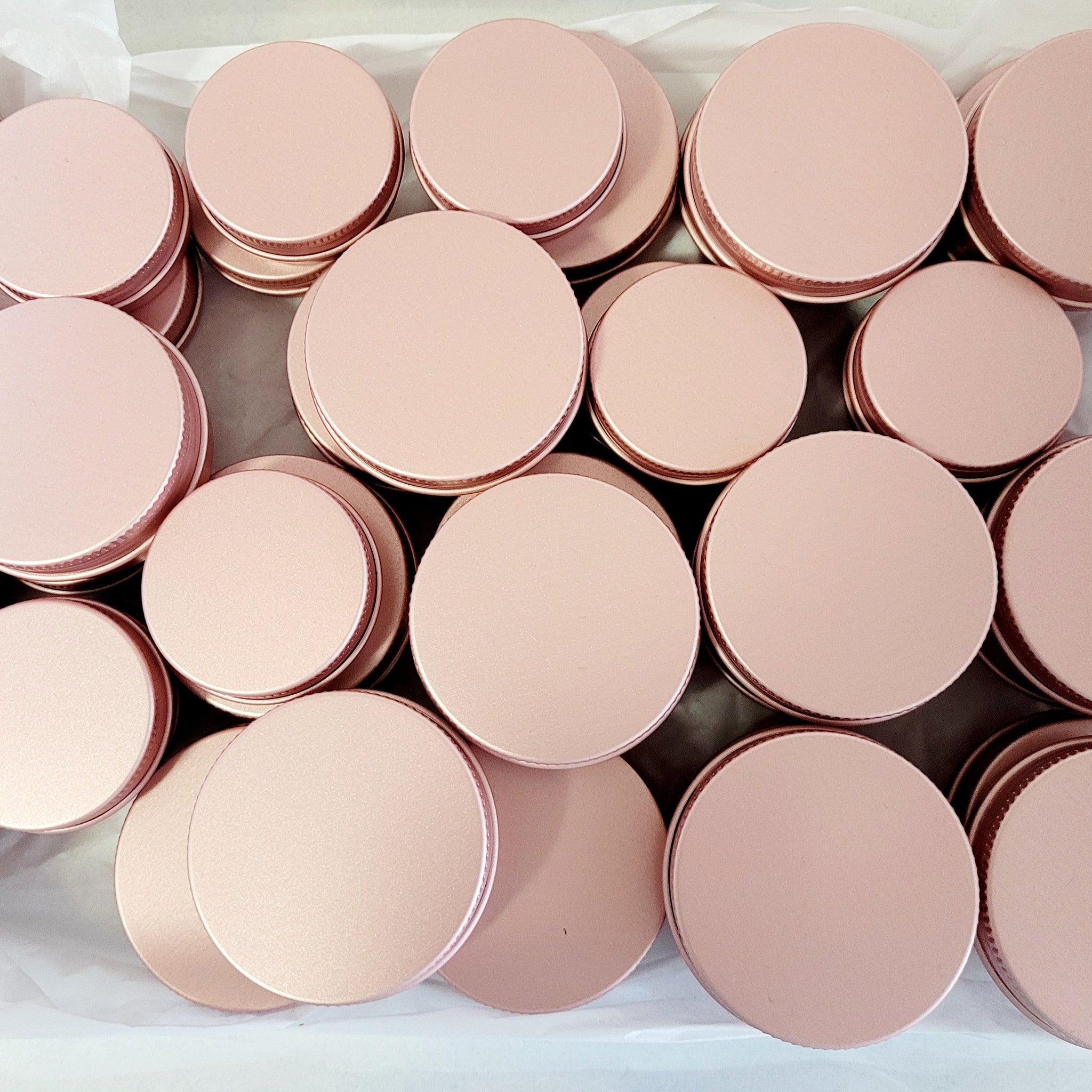 Pink metal jar lids with a circular shape, stacked in a white box