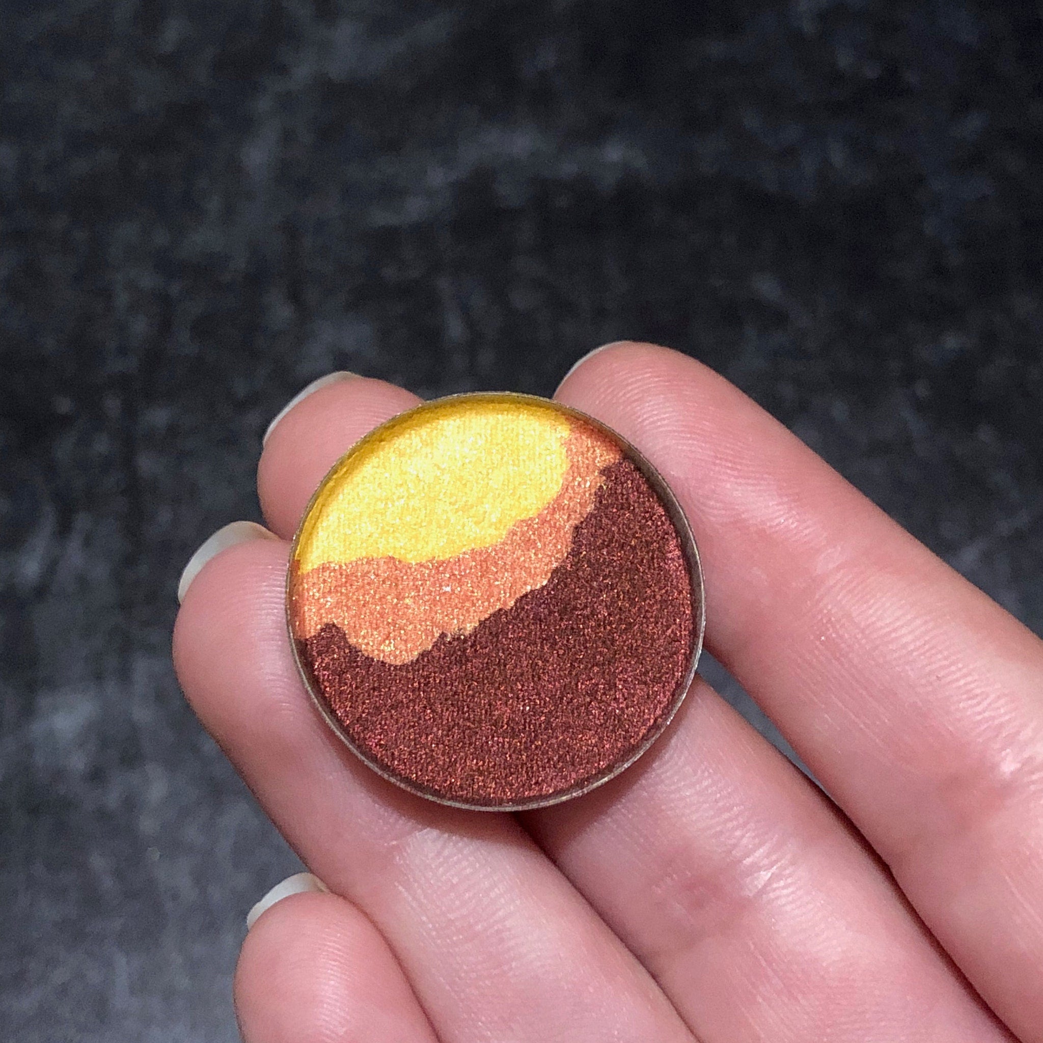 Eyeshadow compact with yellow, orange, and brown metallic colors held in hand