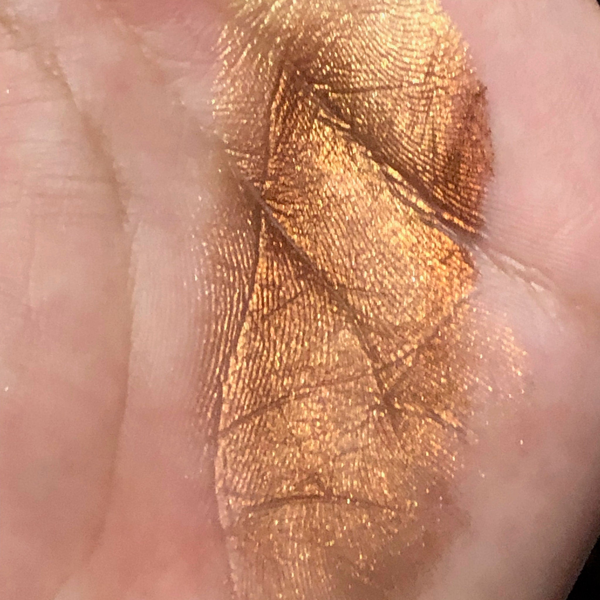 Gold eyeshadow swatch with metallic finish on skin, showing fingerprint detail