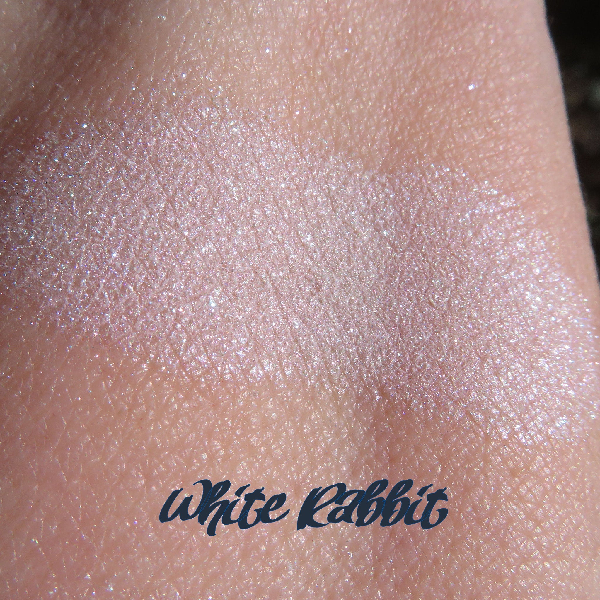 Side view of loose white eyeshadow with violet shimmer in a clear jar, showcasing sparkly glitter particles.