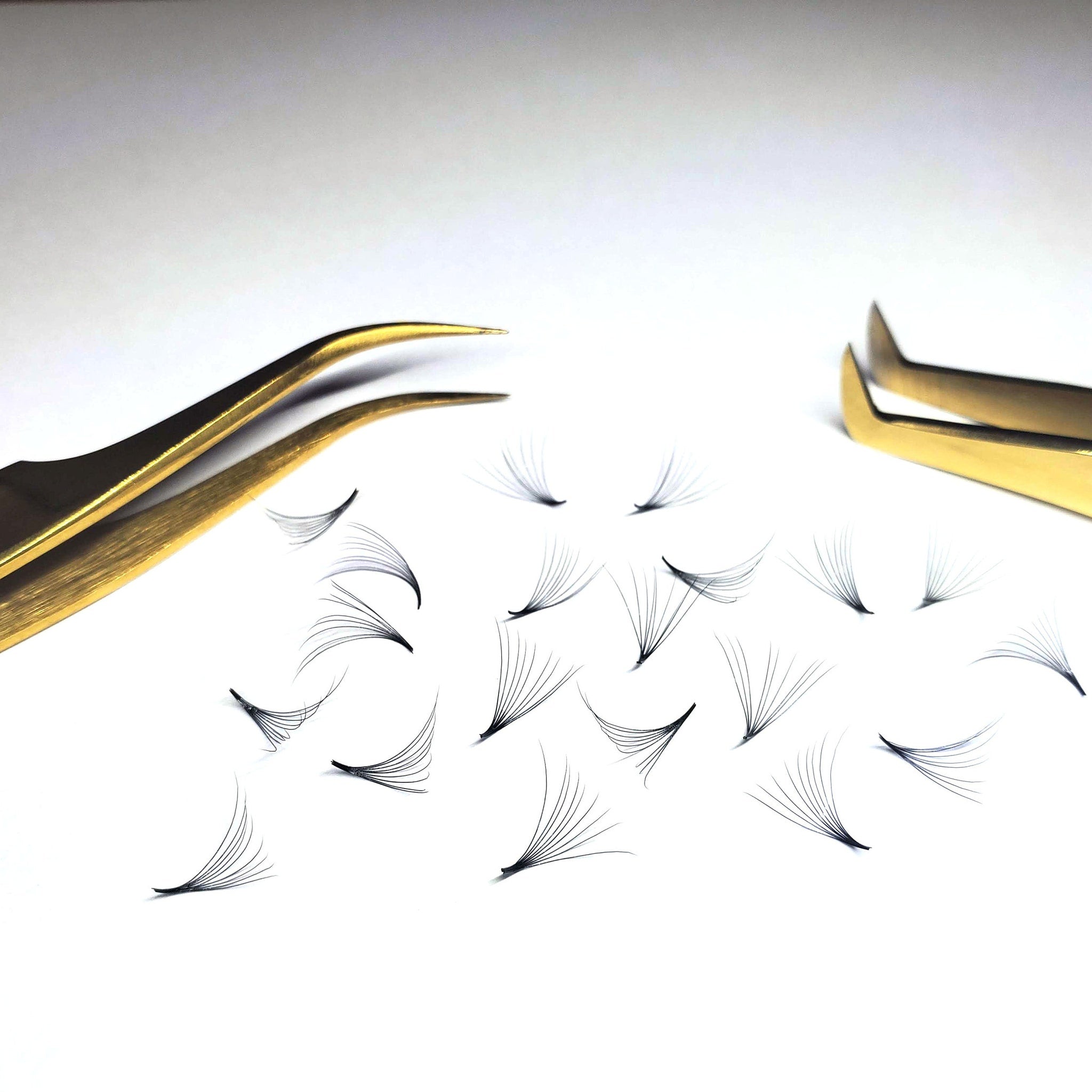 Eyelash extensions with black synthetic fibers, gold tweezers, and white background
