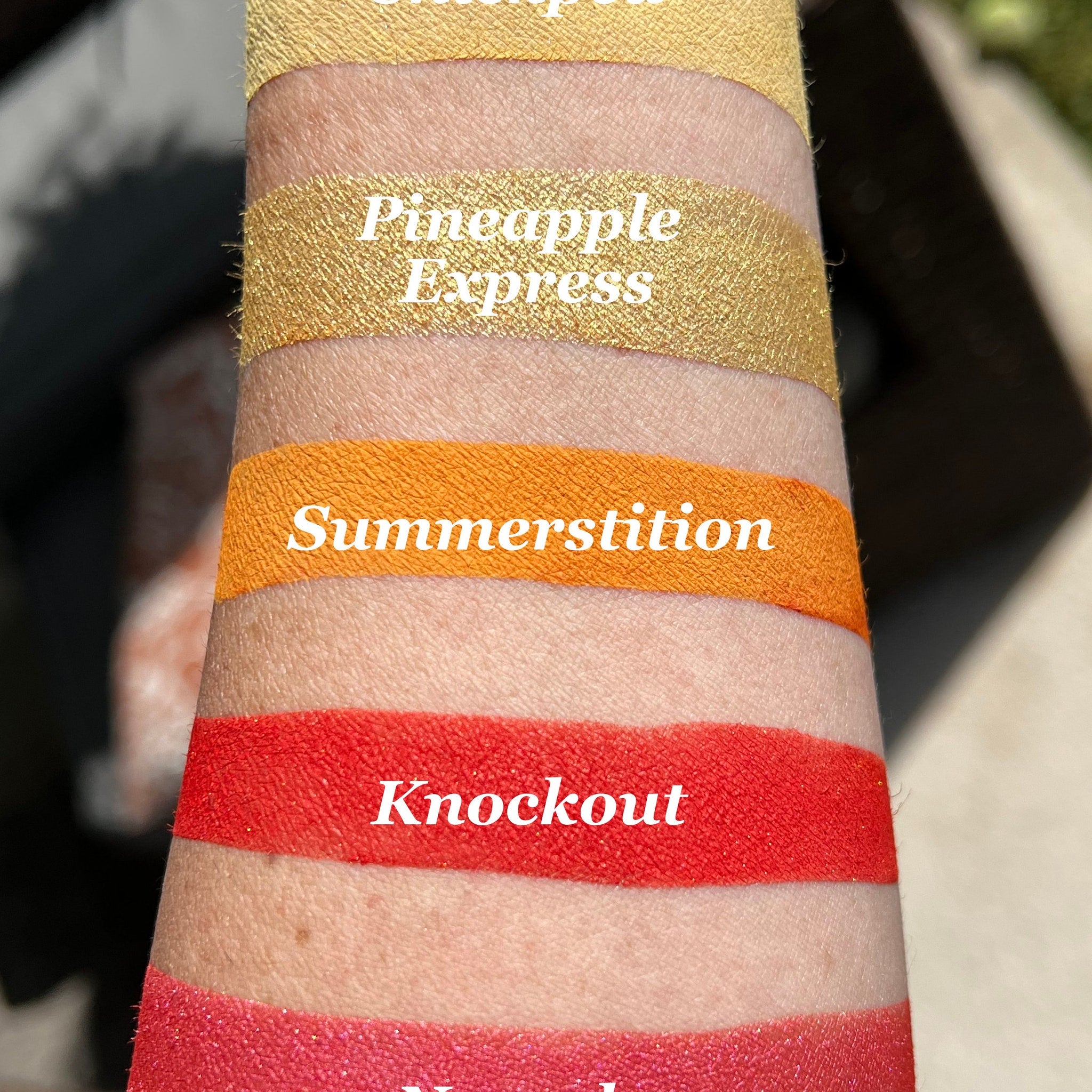 Lip swatch of gold, orange, and red shades on skin, with text labels for each color