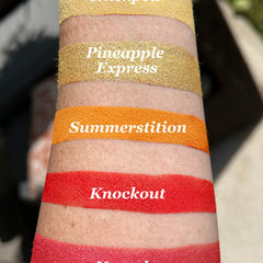 Lip swatch of gold, orange, and red shades on skin, with text labels for each color