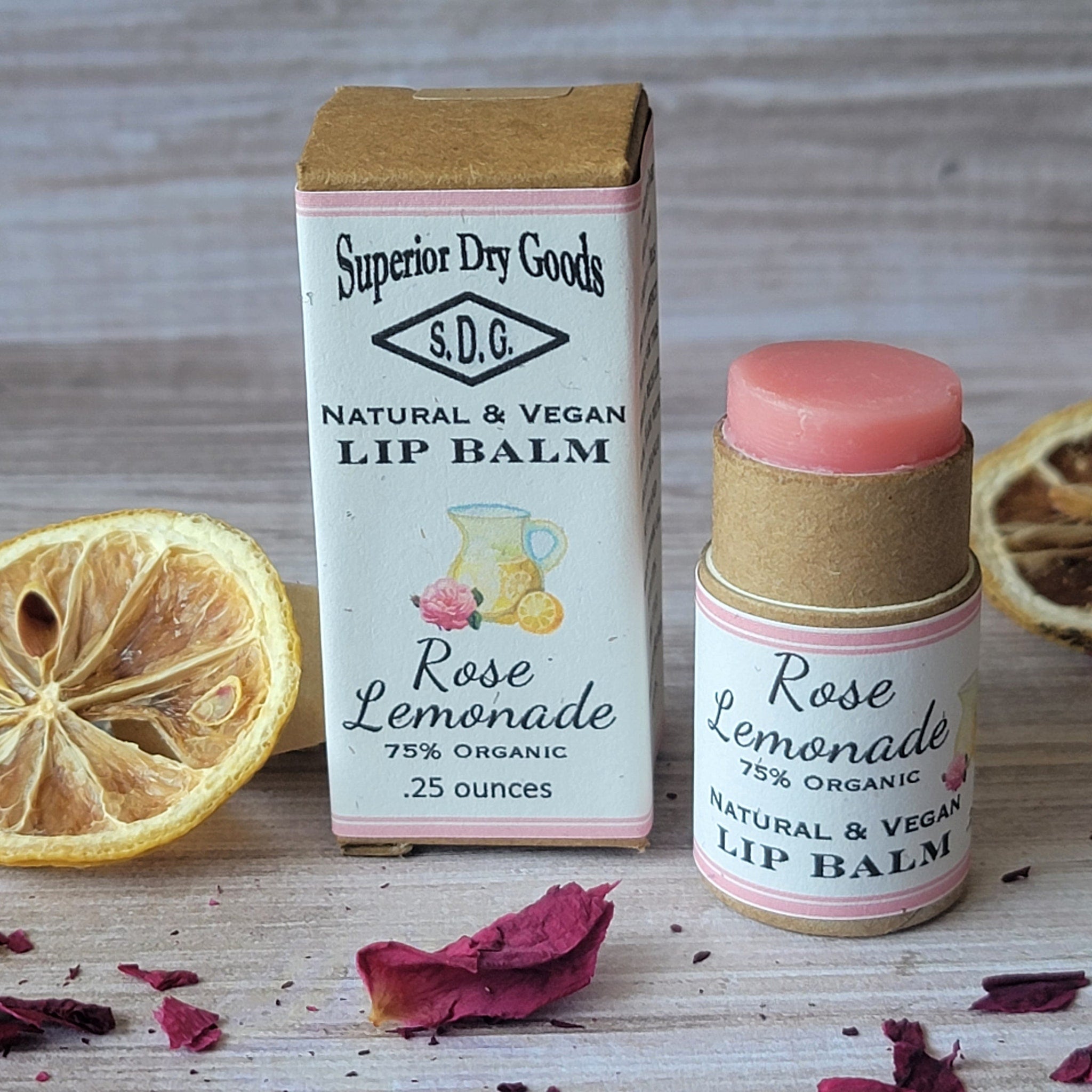 Lip balm in cardboard tube with pink balm, Rose Lemonade label, and dried lemon slice on wood surface