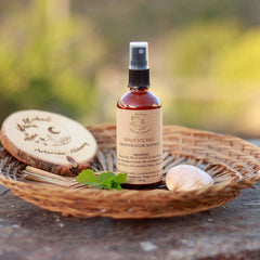 Sunscreen bottle with brown glass, black spray top, and label, in a woven basket with Artemisia Alchemy branding