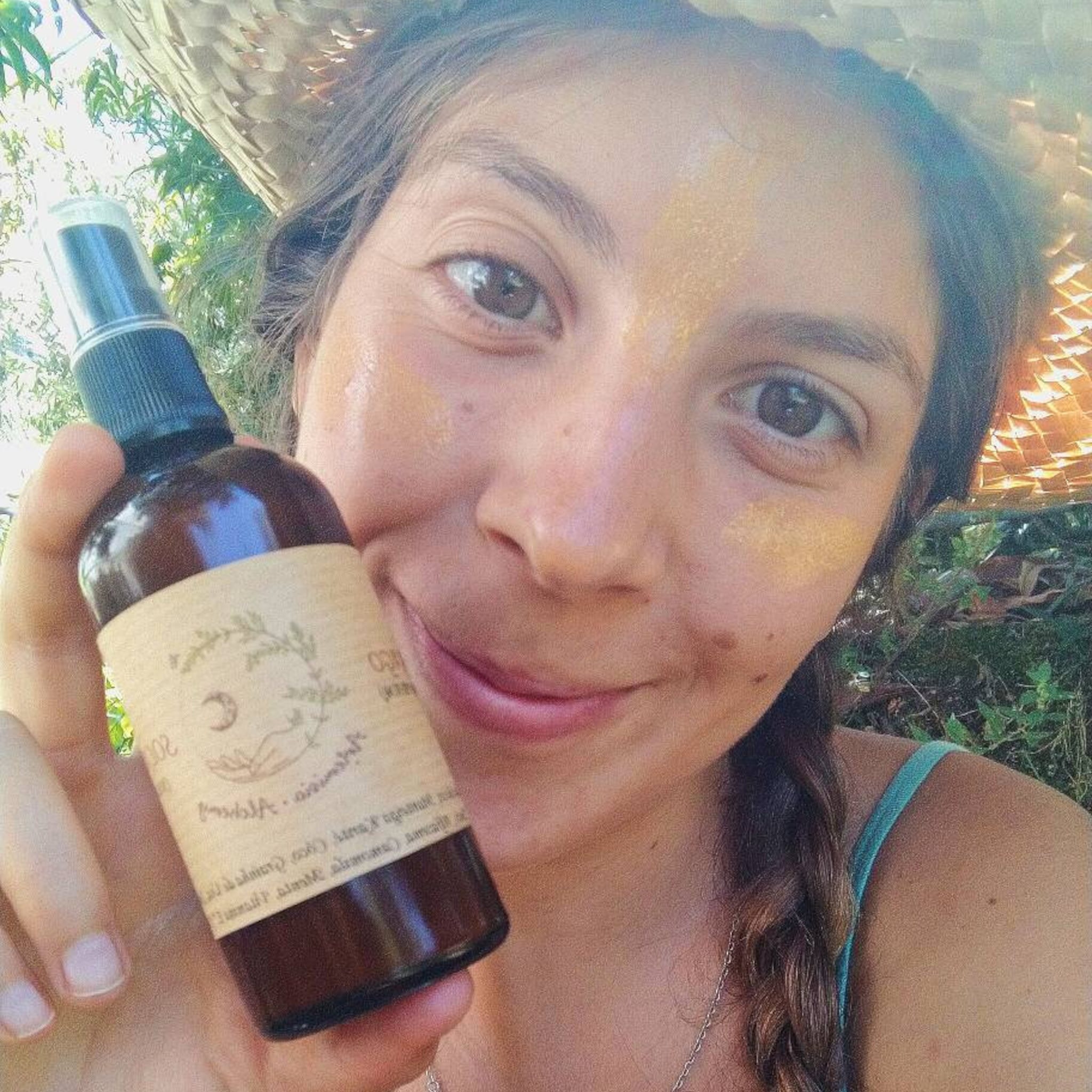 Brown bottle spray with label, held by person with gold face makeup, outdoors