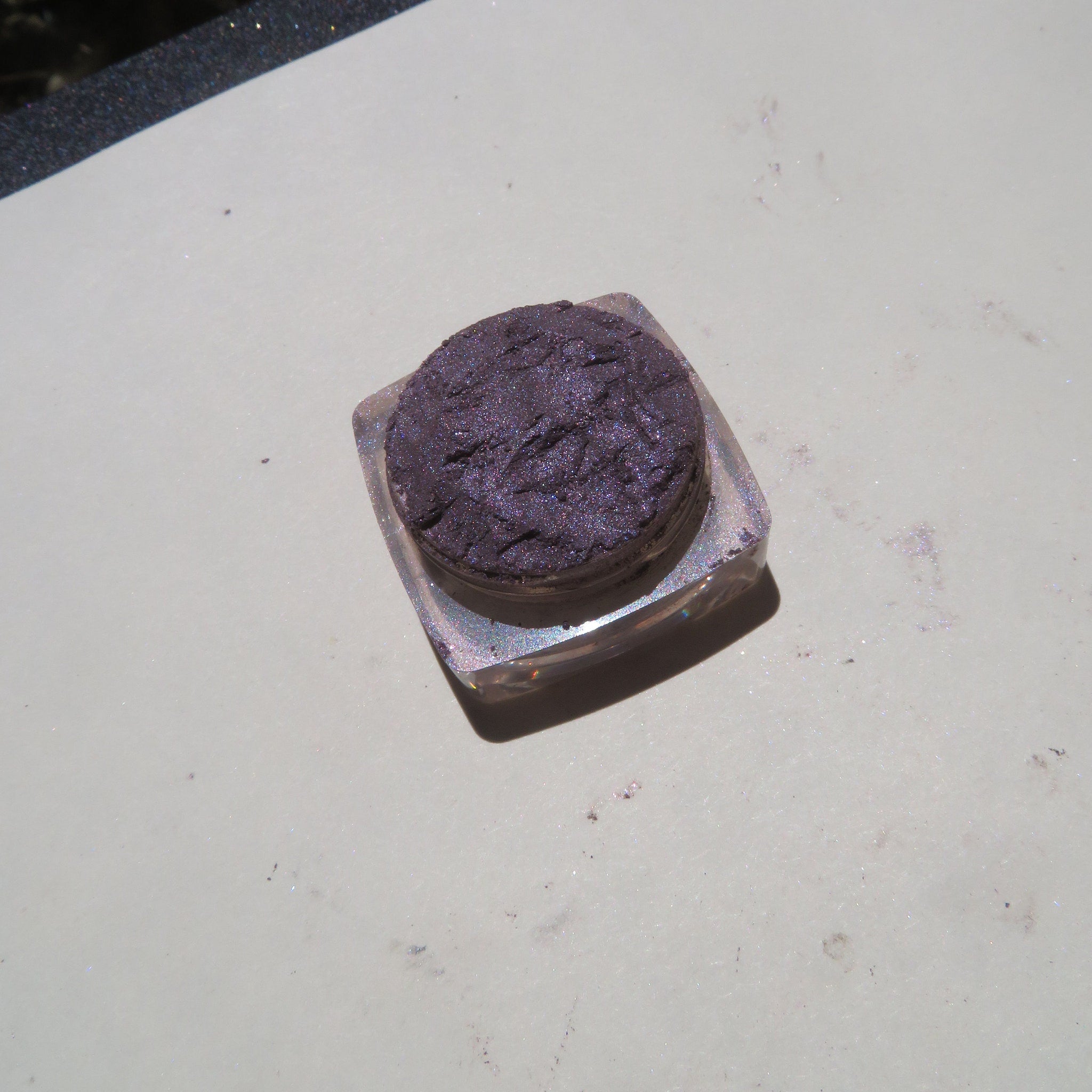 Close-up of loose mineral eyeshadow jar showing dark black purple shimmer powder with eco-friendly packaging