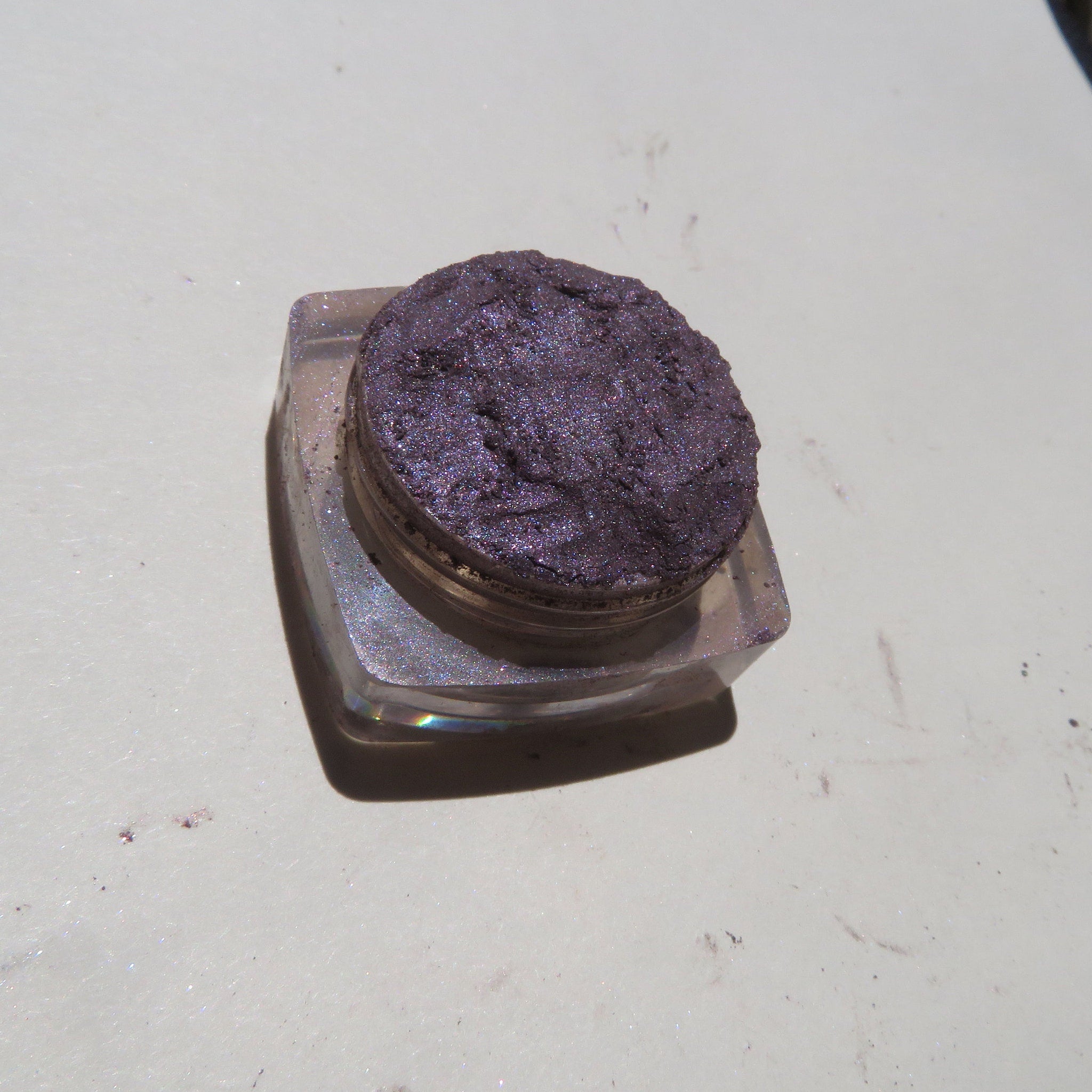 Close-up of loose mineral eyeshadow with dark black-purple shimmer in eco-friendly packaging