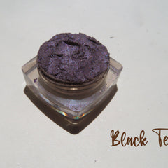 Close-up of loose mineral eyeshadow in dark black purple with shimmer particles, vegan and cruelty-free