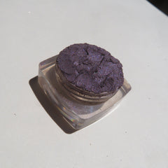 Side view of loose mineral eyeshadow in dark black purple shimmer, showcasing fine powder texture in eco-friendly packaging
