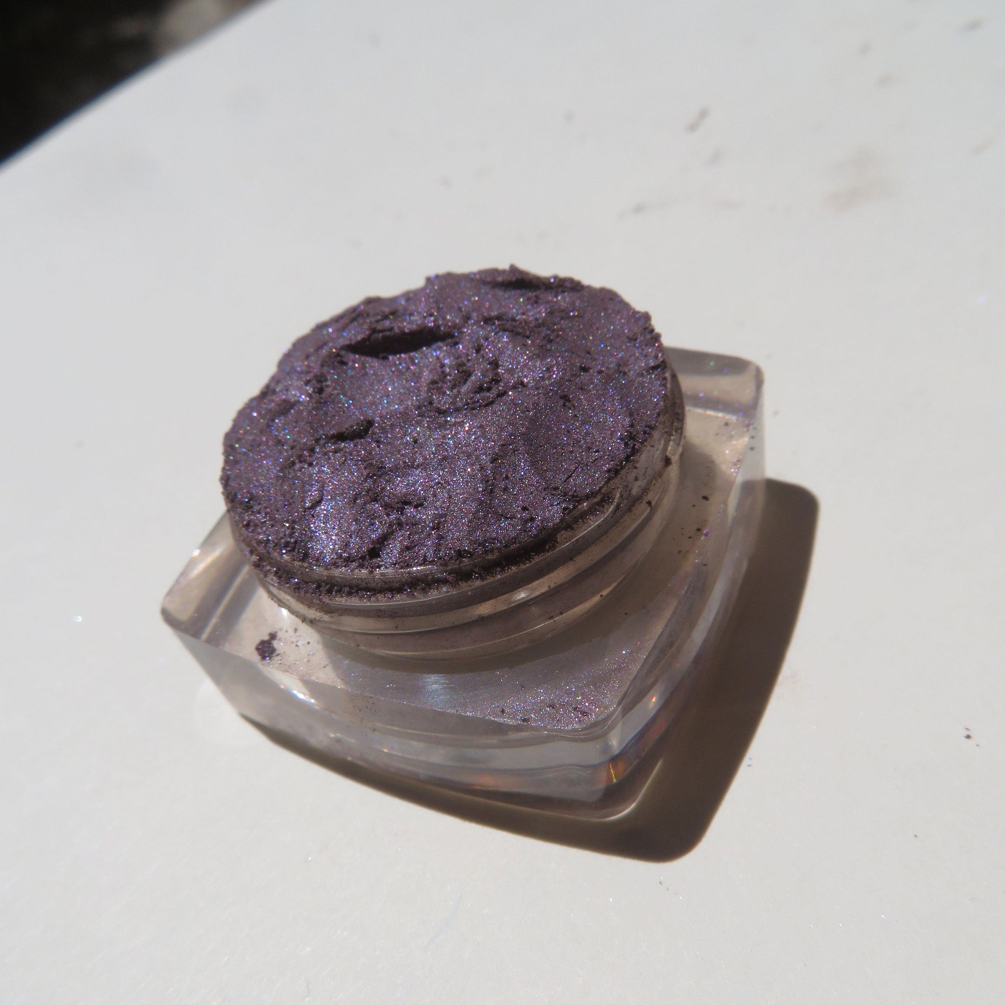 Close-up of loose mineral eyeshadow with dark black-purple shimmer particles in a fine powder texture