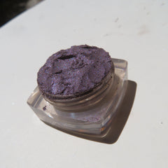 Close-up of loose mineral eyeshadow with dark black-purple shimmer particles in a fine powder texture