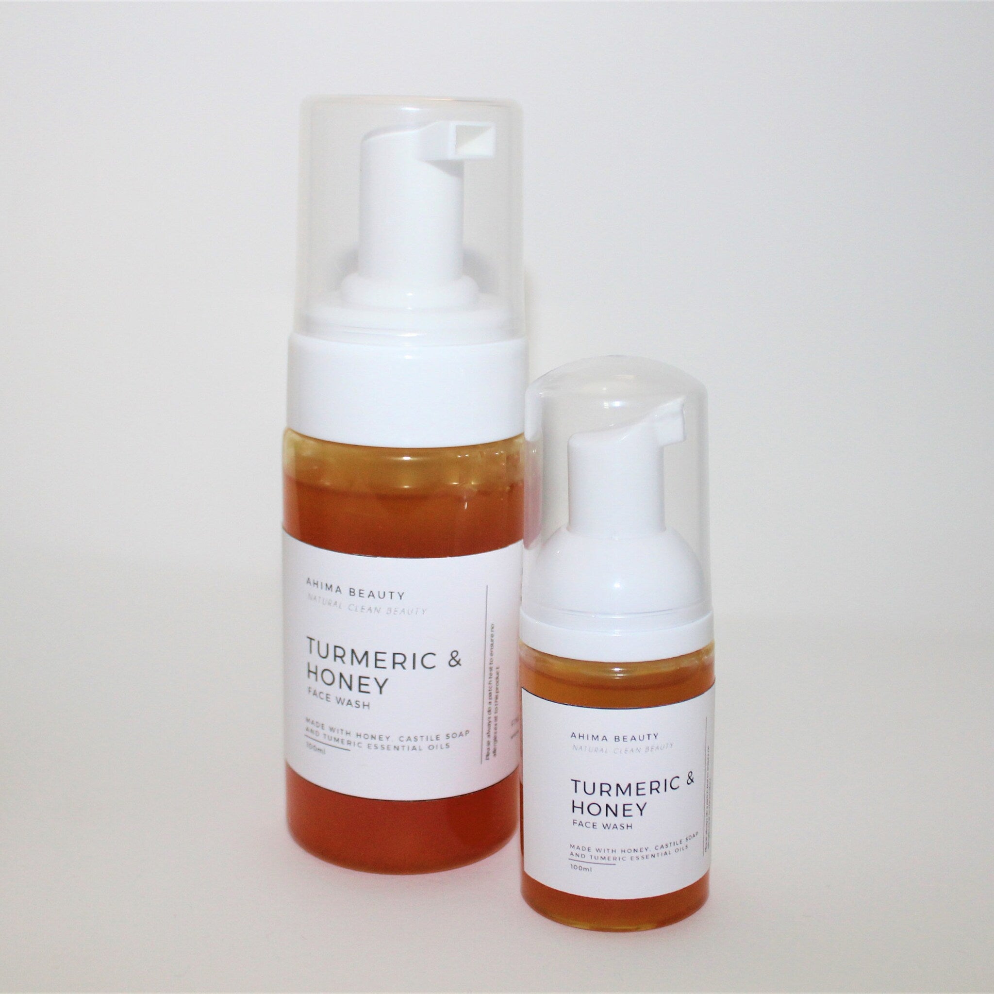 Face wash bottles with white pump tops, clear plastic, and amber liquid, AHIMA BEAUTY label visible