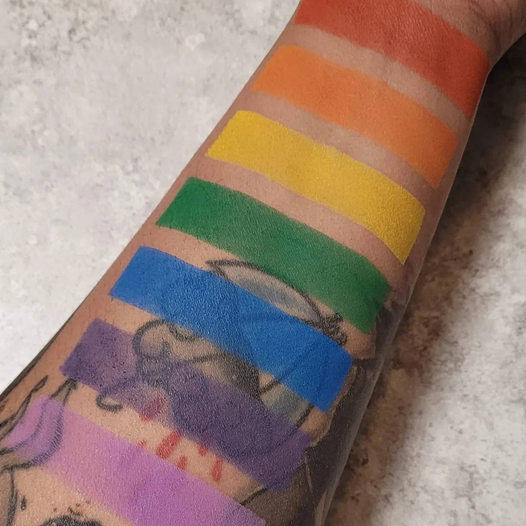 Side view of rainbow pride eyeshadow palette showing seven matte pans in vibrant colors with sleek black case