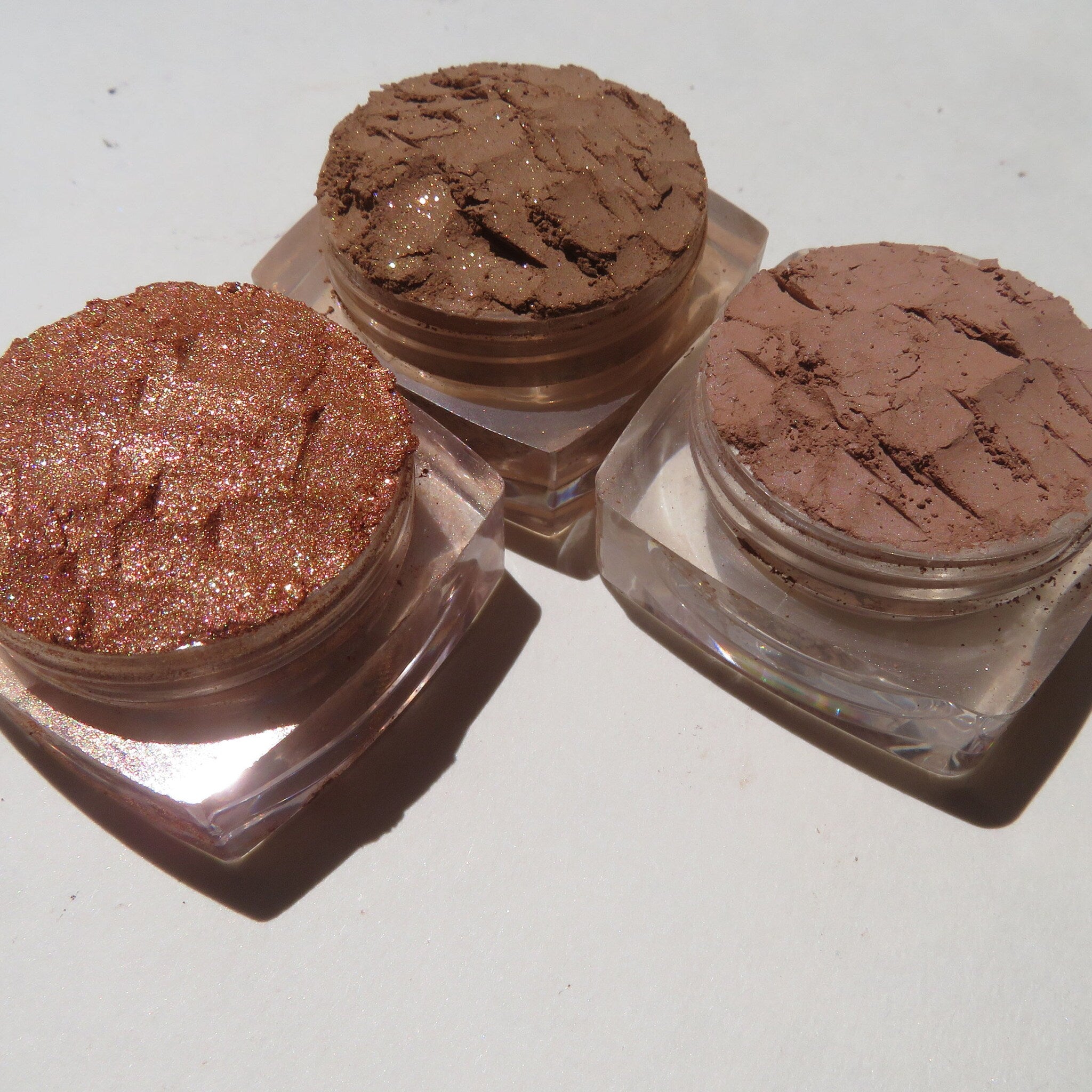 Three square mineral eyeshadow pans in fall brown shades—Basic, Showstopper, and Tigerlily—arranged on a wooden tray.
