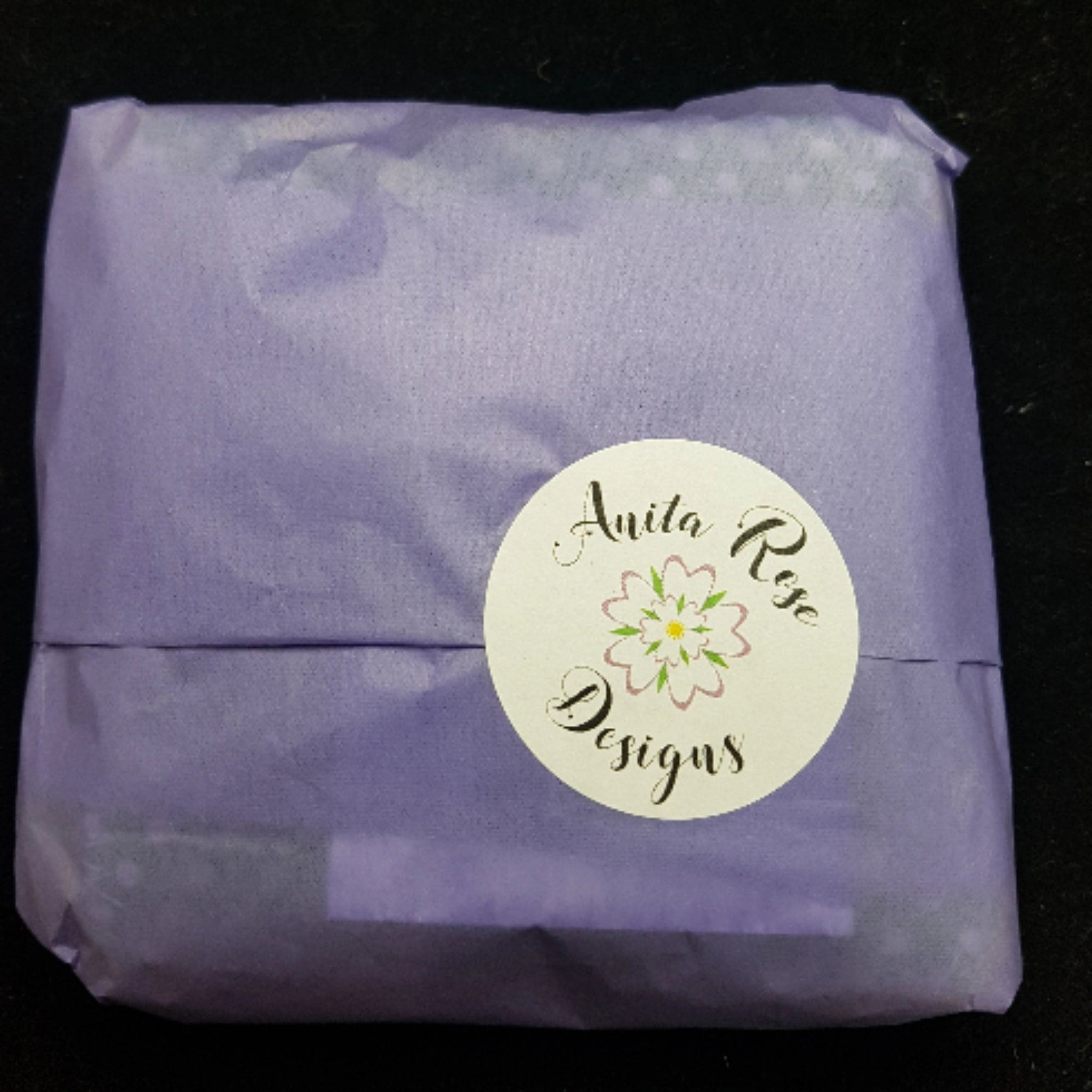 Wrapped gift in lavender tissue paper with Anita Rose Designs sticker on black background