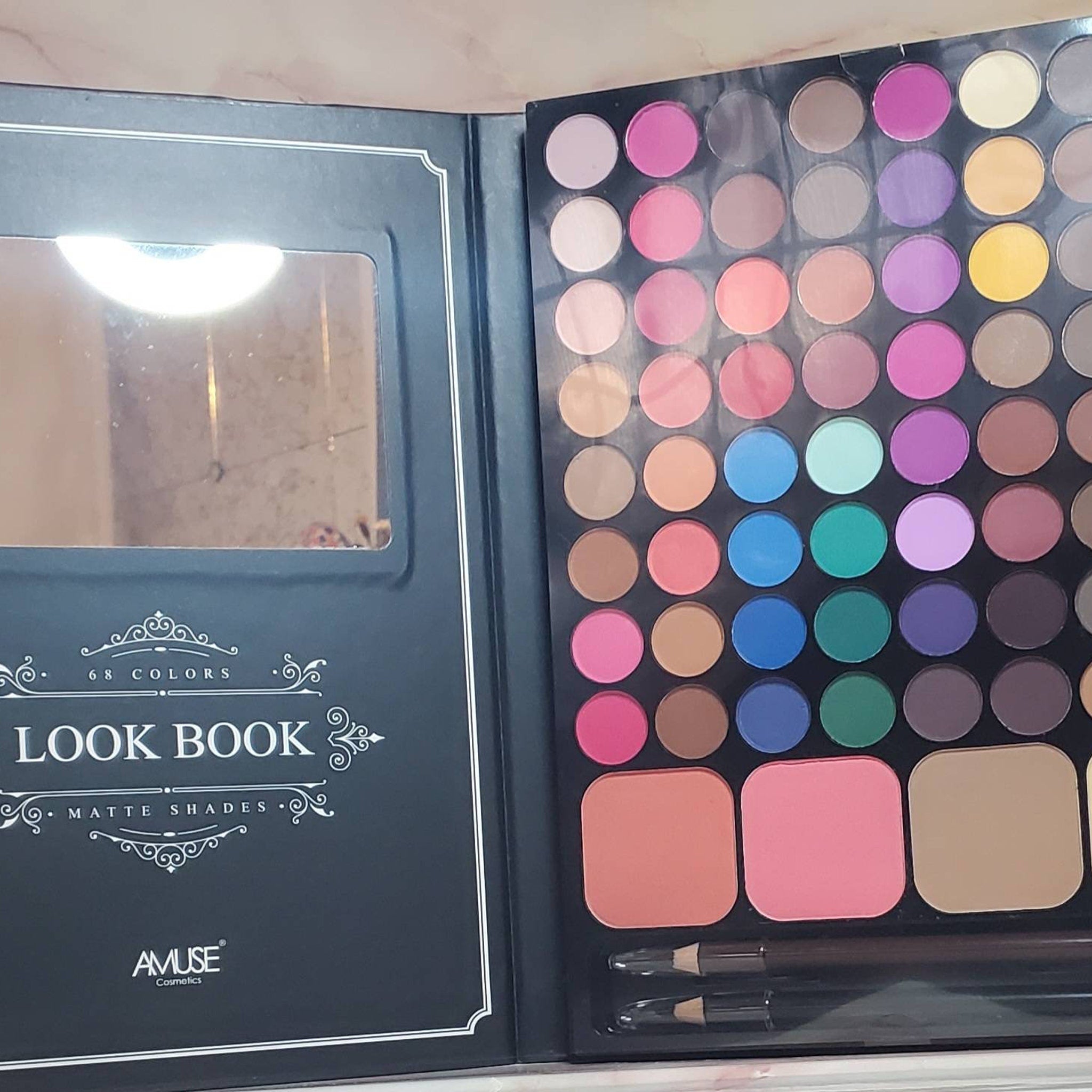 Makeup palette with various color eyeshadows, blush, and applicators, "Look Book" text, and "Amuse" brand