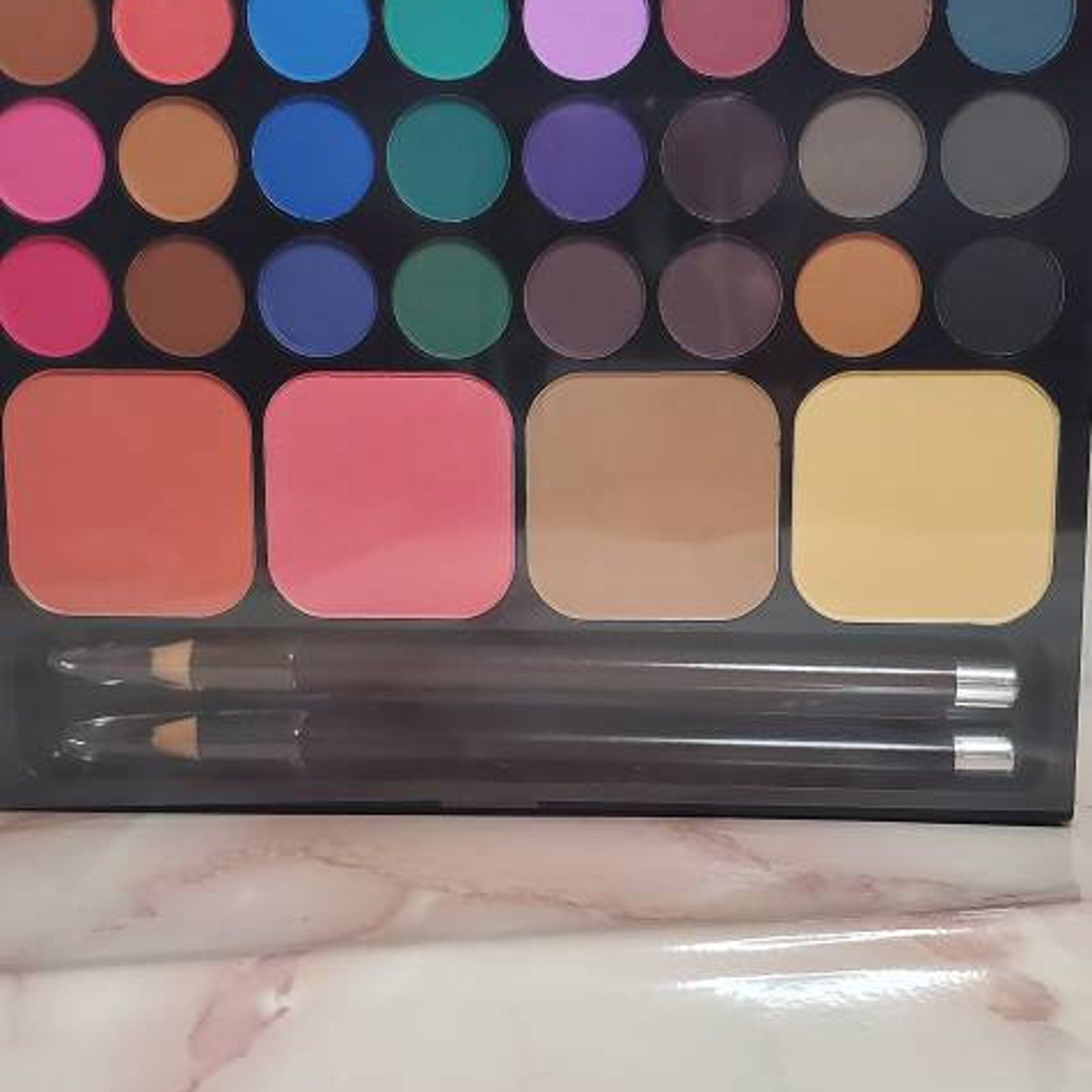 Makeup palette with various colorful eyeshadows, blush, and two black eyeliner pencils