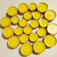 Yellow balm in pink metal tins, arranged in a circular pattern on a light surface