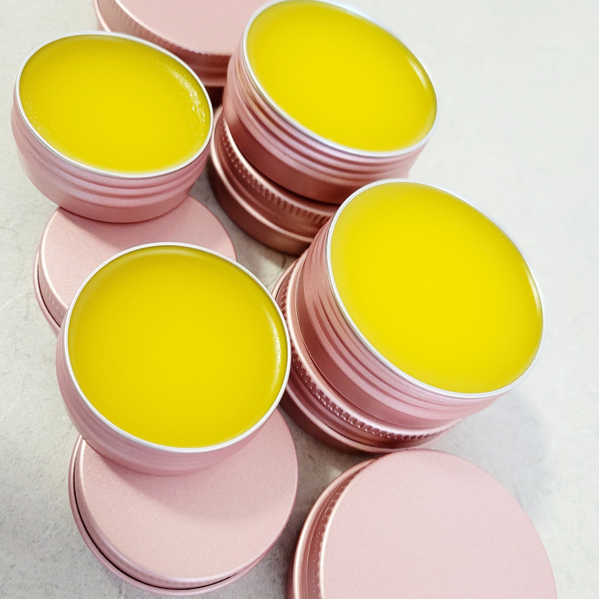 Lip balm in pink metal tins with yellow balm visible, close up shot