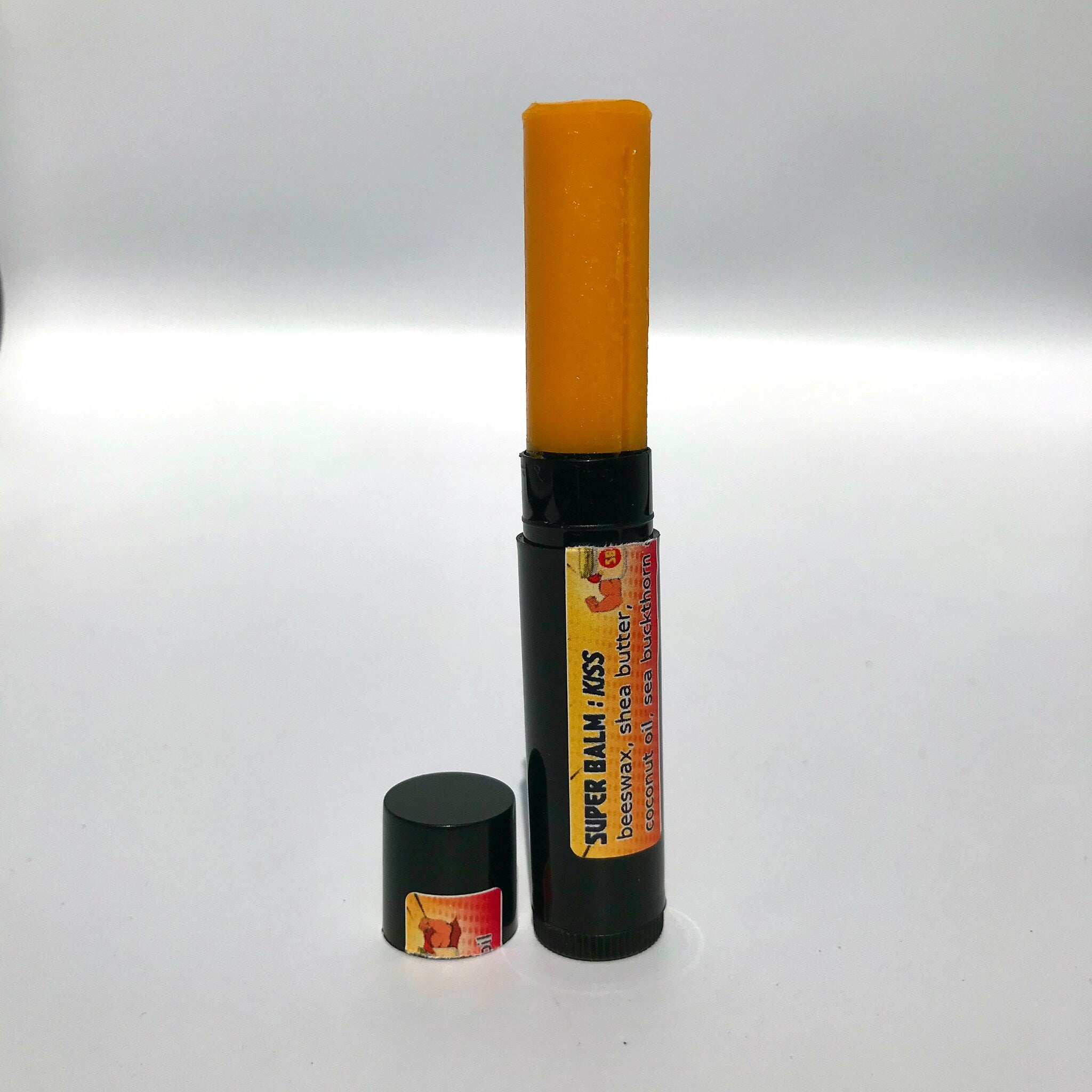 Lip balm stick with orange balm, black tube, and "SUPER BALM : KISS" label visible