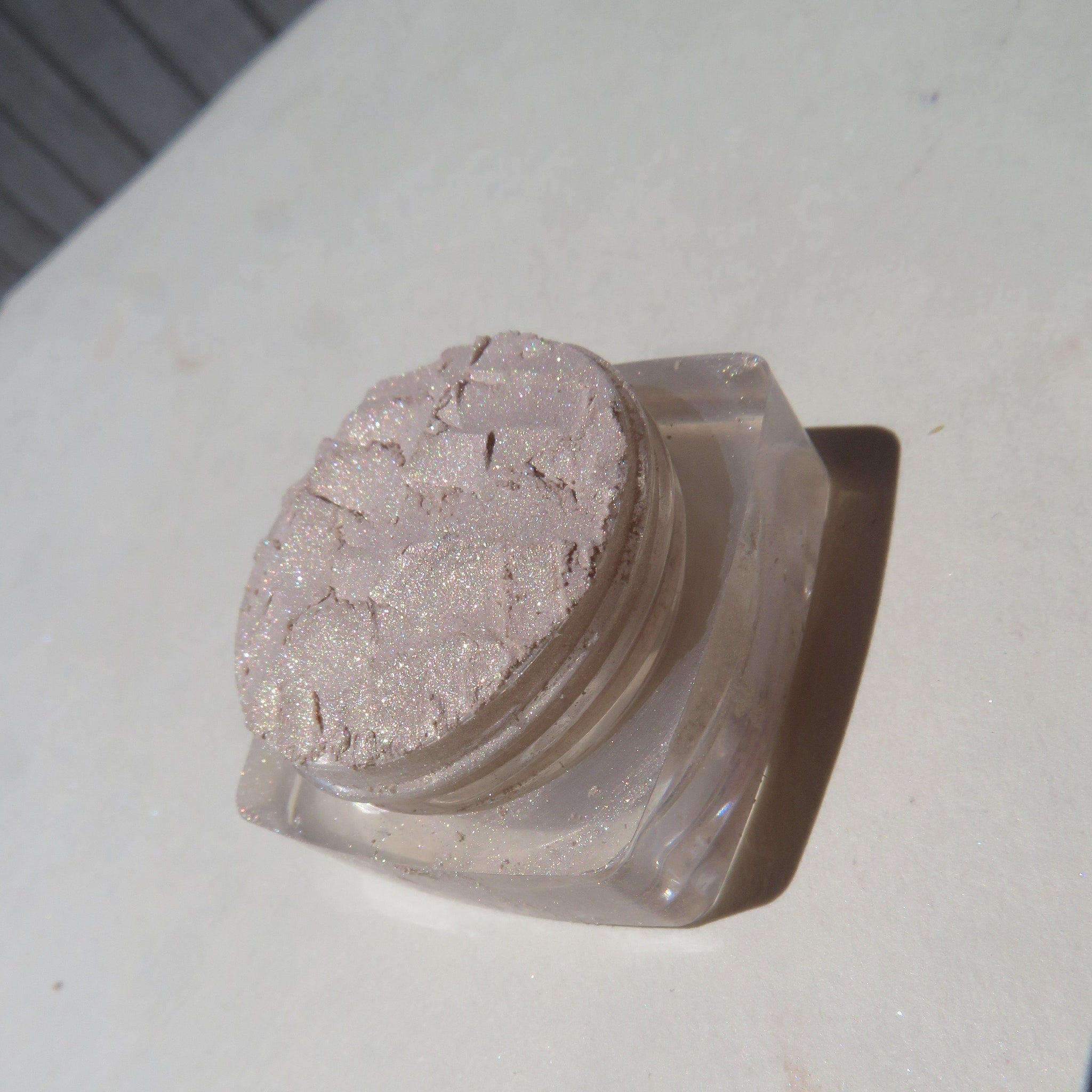 Side view of loose mineral eyeshadow in pale yellow shimmer with golden flecks, showcasing texture and sparkle