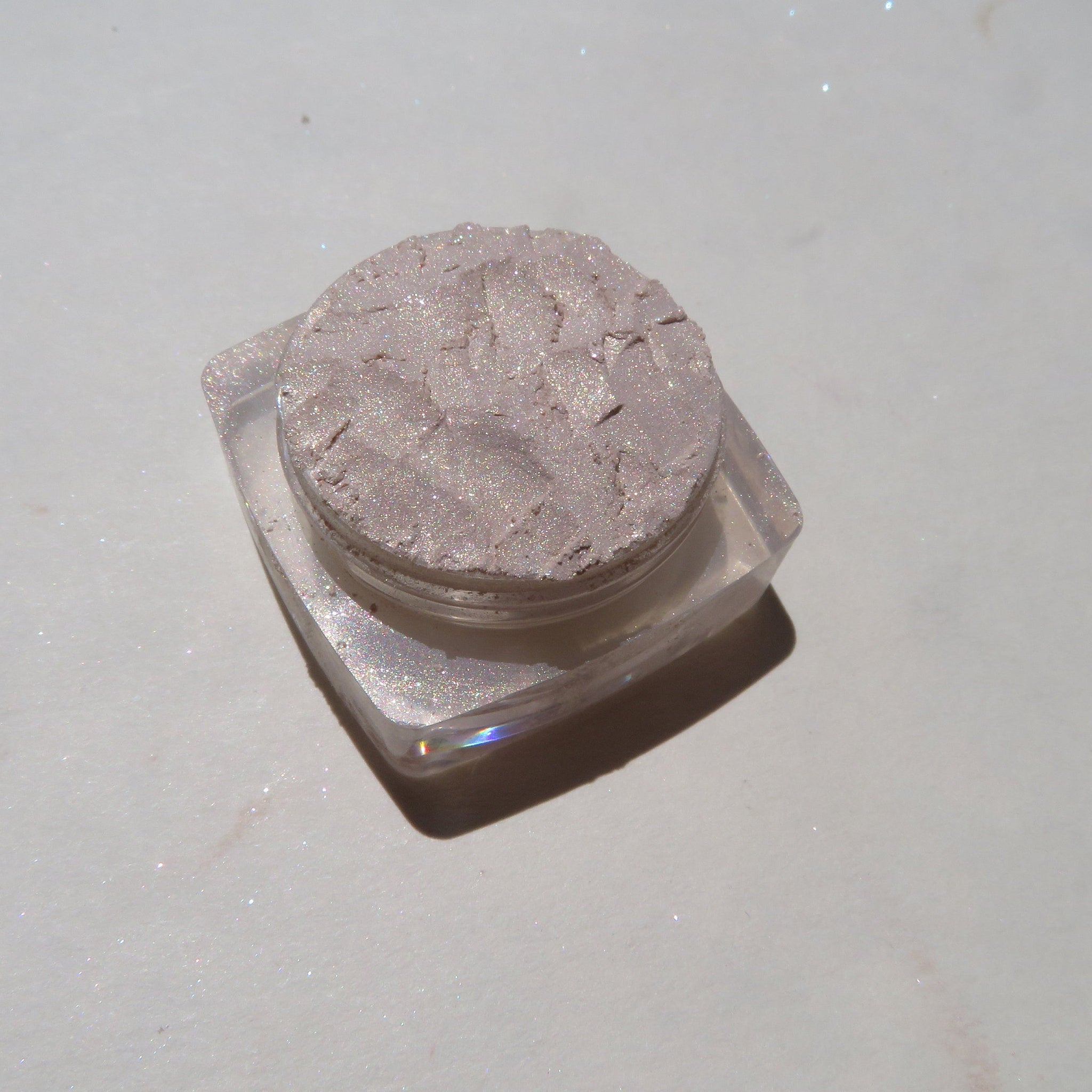 Side view of loose mineral eyeshadow in pale yellow shimmer with golden sparkles, showcasing texture
